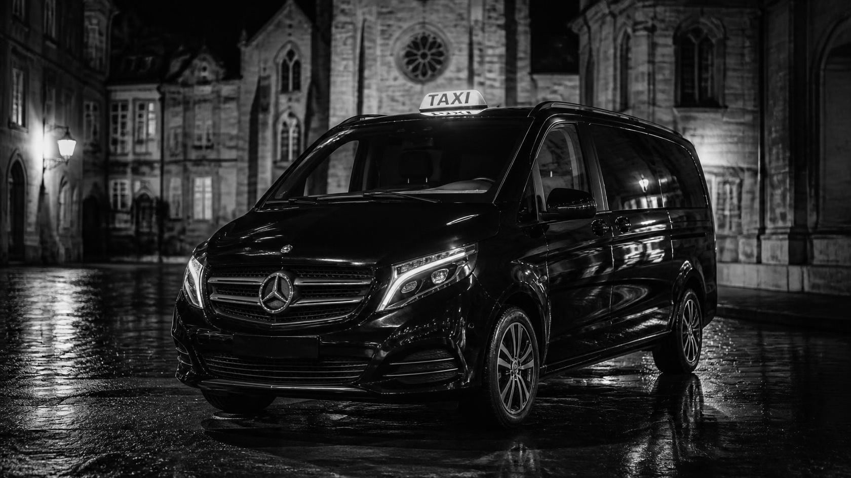 Van noir avec lumineux taxi, de nuit sur des pavés mouillés